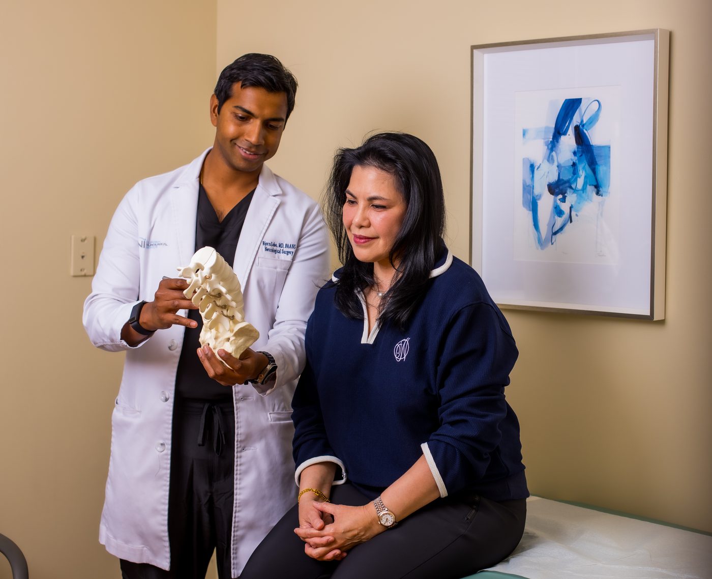 Dr. Bjorn Lobo explaining a spinal anatomy model to a patient during a consultation